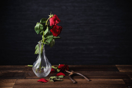暗灰色背景下凋谢的玫瑰,木桌上摆着秋天的花瓣和树叶,设计理念是悲伤