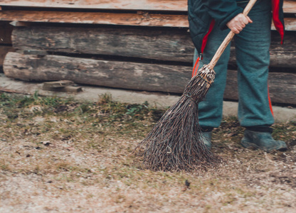 一个村子里的女人用桦树扫帚打扫她家附近的院子。
