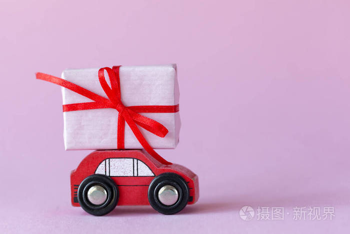 粉红色背景的车顶上有一个礼品盒的微型红色汽车情人节概念
