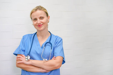 A nurse with blond hair and a stethoscope in uniform is smiling 