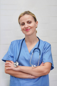 A nurse with blond hair and a stethoscope in uniform is smiling 