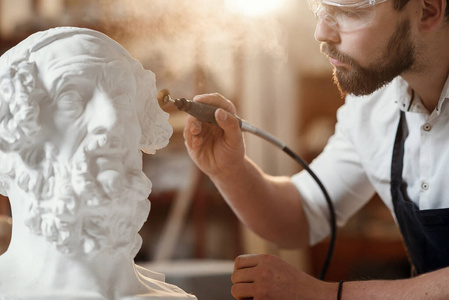 男雕塑家在创意艺术工作室的工作场所修复女性头部的石膏雕塑。
