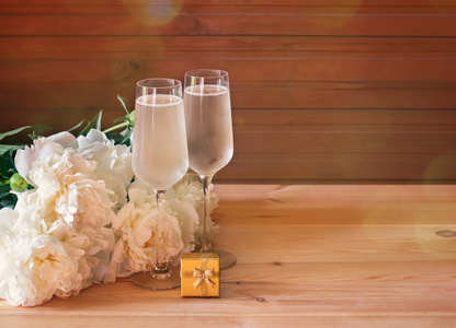 Two glasses of champagne, gold gift box and white peony flowers 