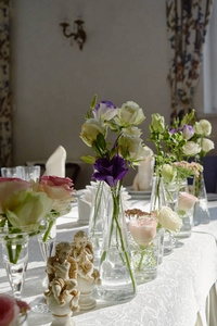 餐厅婚礼桌上美丽的花卉布置，复制空间。一束粉红色的玫瑰，紫色的桔梗和绿色的玻璃花瓶