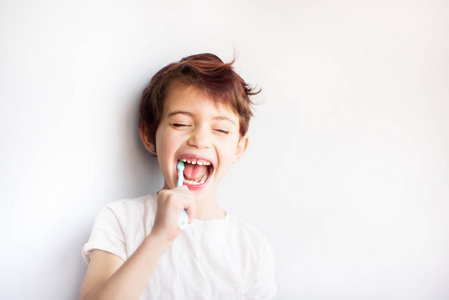 闭眼儿童用蓝白牙刷刷牙的水平肖像。从小就有牙科和医疗保健。笑脸换牙健康。复制文本空间
