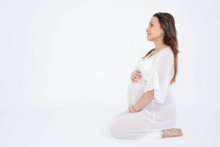 从侧面看,这名身着白色内衣的深色孕妇正坐在地上,抱着肚子.