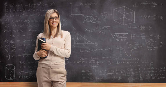 Young female teacher in front of a school blackboard smiling 