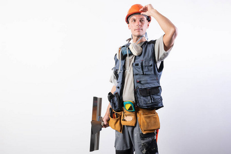 建筑工人用抹刀。抓住头盔向前看。穿着工作服，戴着安全帽。在浅灰色的背景上。