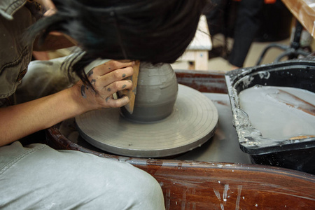 女孩坐在陶工的轮子旁，创造了一罐陶瓷。陶工在机械圈后面用粘土做陶器