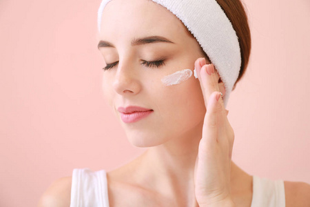 美丽的年轻女子在彩色背景下涂面霜照片