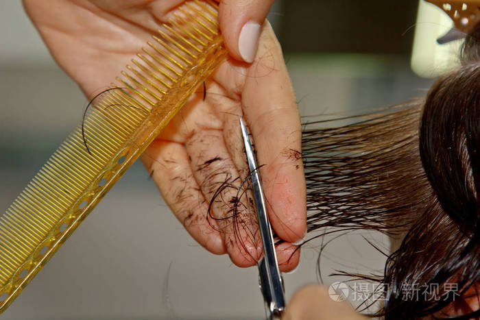 理发师的特写镜头在沙龙里剪下顾客湿棕色的头发.理发师给女人理发.