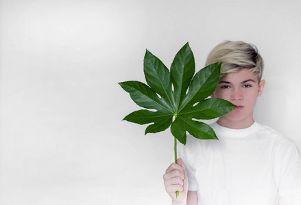 a teenage boy holds a large leaf from a tree in front of him 