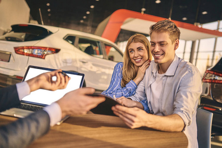 Handsome man and cheerful girl buying a car in showroom. 