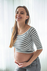 幸福的大肚子孕妇在窗边。怀孕和家庭的概念