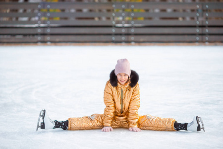 一个可爱的小女孩跌倒后穿着溜冰鞋坐在冰上