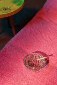 Ashtray with burning cigarette on sunbed with yellow table with 