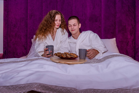 一个女孩和一个年轻人，新婚夫妇躺在一张大床上吃早餐。