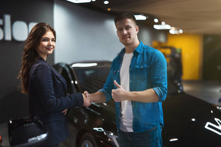 年轻积极的女经理身着西装在电动车经销中心与满意的男士客户握手，专业成功合作