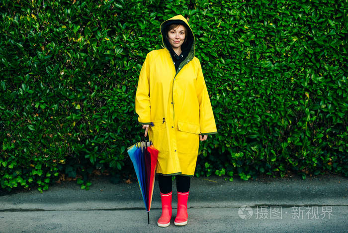 女孩穿着黄色雨衣背着伞站在绿色的墙上