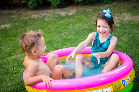 在炎热的夏天，两个小弟弟和妹妹在游泳池里嬉戏嬉戏。孩子们在儿童游泳池游泳。两个活泼可爱的孩子在后院的充气池里嬉戏玩耍