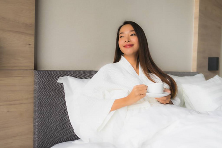 在床上放着咖啡杯的美丽的亚洲年轻女性肖像