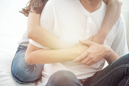 年轻的亚洲情侣女孩背着男人从床上背起,浪漫的亚洲人坐在床上拥抱