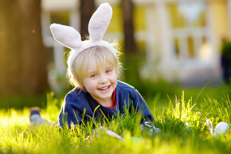 复活节那天，戴着兔子耳朵的漂亮小男孩在春天公园里寻找复活节彩蛋。