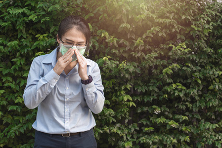 病态的年轻亚洲妇女打喷嚏隔离面具在绿色围栏背景.