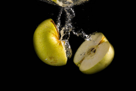 落入水中的水果一个半绿色的苹果垂直落入水中,黑色背景上有飞溅和