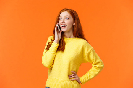 开心而惊讶的红发女孩睁大了眼睛，在电话中听到朋友的好消息，把智能手机放在耳边，交谈，橙色背景