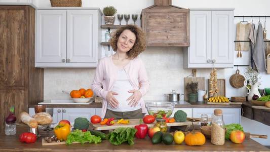 孕妇抱着肚子在厨房里做新鲜的有机健康食品。