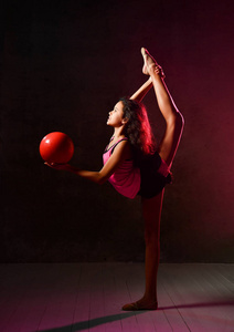 年轻的女体操运动员用红球做体操，在黑暗中进行垂直劈叉伸展