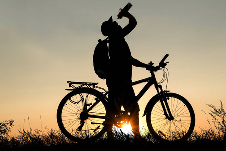 夕阳下骑着自行车喝水的人的侧影