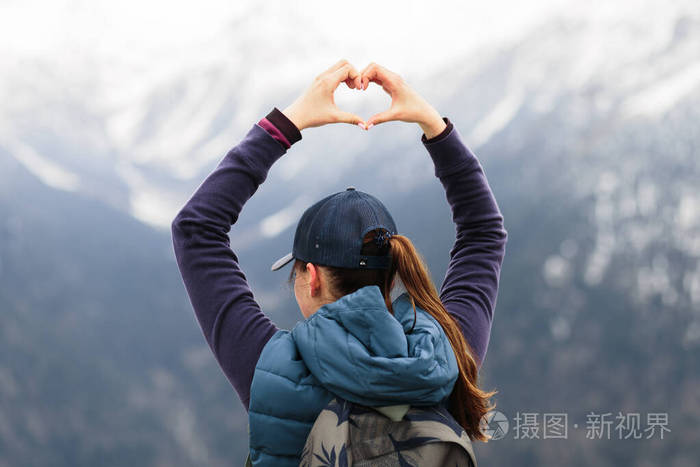 一位年轻的女旅行家站在山顶上，用手展示了一颗心