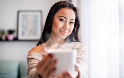 在家的亚洲女人手里的一杯茶或咖啡