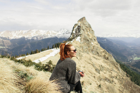 一个年轻的女孩摄影师和旅行者坐在山顶的草地上