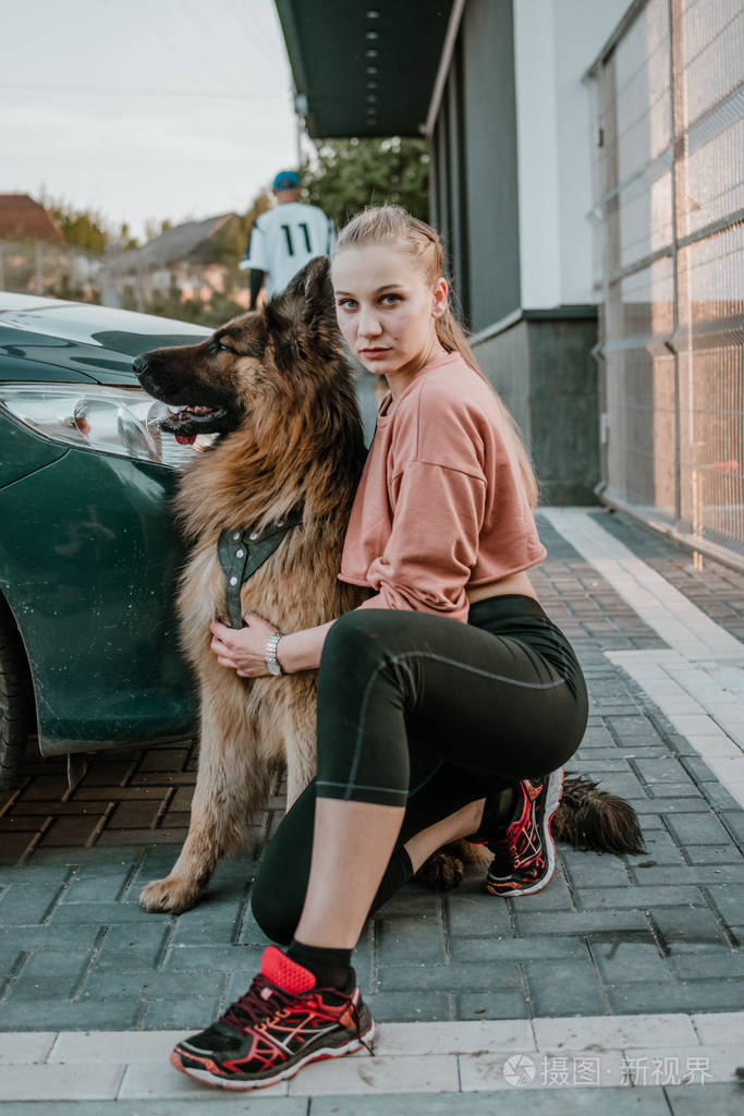 年轻漂亮的运动女孩和毛茸茸的德国牧羊犬大狗在城市街道上玩耍宠物