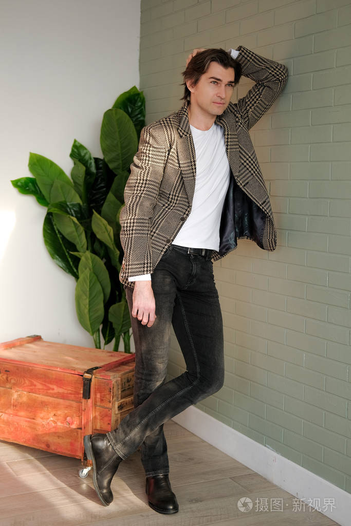高大英俊的男人站在灰色的墙壁和木箱旁照片-正版商