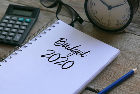 计算器.眼镜时钟，铅笔和笔记本写着2020年预算在木制背景上。