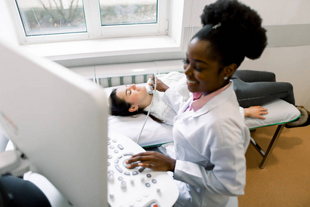 一位迷人的年轻女子在现代诊所接受非洲女医生的甲状腺超声扫描检查