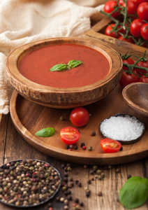 木制盘子，奶油番茄汤放在圆形托盘上，胡椒粉和厨房布放在木制背景上，再放一盒生西红柿。