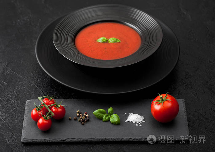 Black restaurant plate of creamy tomato soup on black table back