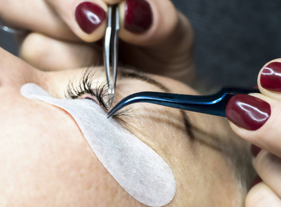 Gluing artificial eyelashes with tweezers. Cosmetic procedure. 