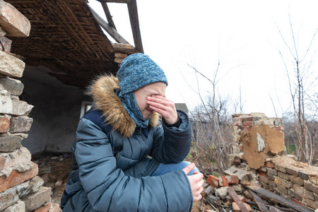 一个少年坐在一座被摧毁的房子的石头上,为因军事冲突而失去亲人而