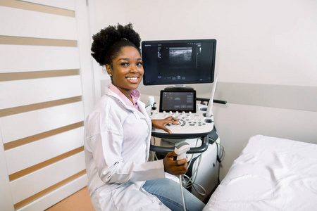 面带微笑的非洲女医生手拿超声波扫描仪，在诊所的灯光室里操作现代超声波扫描仪。四维超声扫描机操作员肖像
