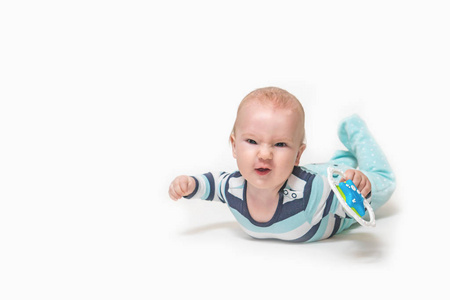 Grinning baby boy is lying on white background holding a toy. 