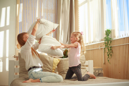 Mother and daughter joyfully play together with pillows at home 