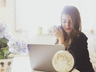 美丽快乐的女人在家里用笔记本电脑工作。年轻女性