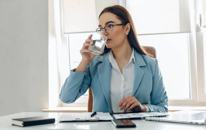 办公室里年轻漂亮的女人一边工作一边喝水