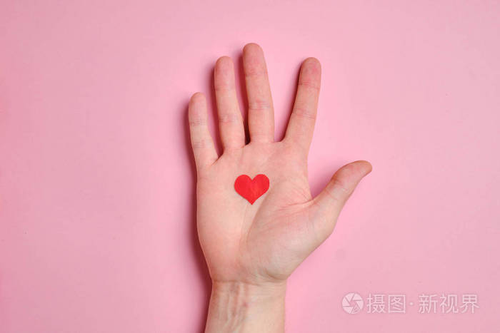手掌上有一个红色的小心形背景是粉红色的纸